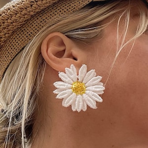 May include: A woman wearing a straw hat and a white blazer with a white daisy flower earring.