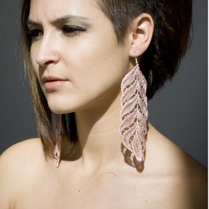 May include: A woman with short brown hair styled in a mohawk with one side shaved. She is wearing large pink feather earrings.