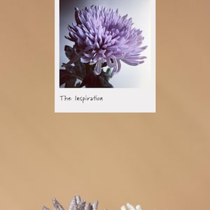 Puede incluir: Fotograf&iacute;a de una flor de crisantemo morada en un marco blanco con el texto "The Inspiration". Debajo del marco, dos accesorios decorativos para el cabello con forma de flor, uno gris y otro blanco.