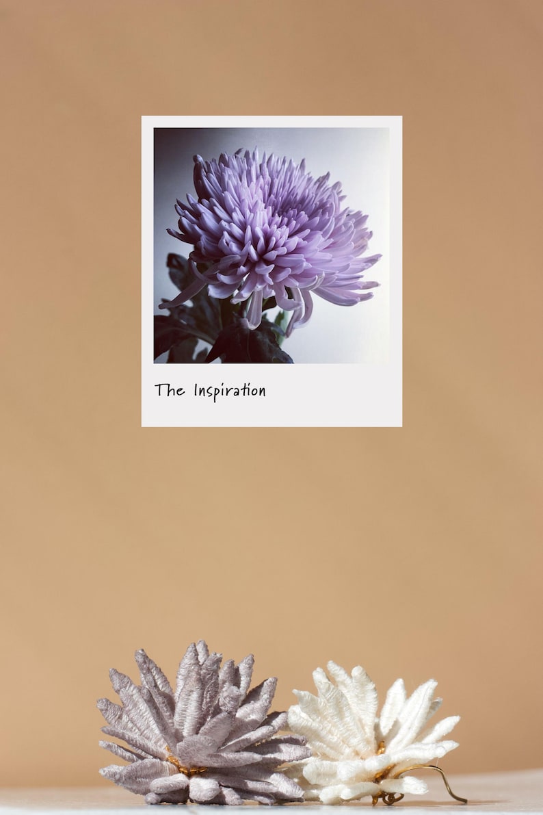 Puede incluir: Fotograf&iacute;a de una flor de crisantemo morada en un marco blanco con el texto "The Inspiration". Debajo del marco, dos accesorios decorativos para el cabello con forma de flor, uno gris y otro blanco.