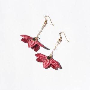 May include: A pair of gold earrings with a pink flower design. The flowers are made of fabric and have a delicate, layered look.