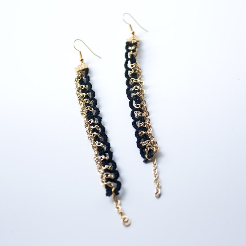 Puede incluir: Un par de pendientes largos y colgantes con eslabones de cadena negros y dorados. Los pendientes est&aacute;n hechos de tela negra y metal dorado.
