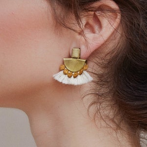 May include: Gold and white tassel earrings with a geometric design. The earrings are made of metal and have a fringe of white tassels.