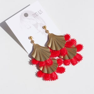 Peut inclure: Boucles d'oreilles dorées avec des franges de pompons rouges. Les boucles d'oreilles présentent un design de coquille superposé.