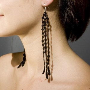 Peut inclure: Boucles d'oreilles en macramé noir avec un design long et pendant. Les boucles d'oreilles présentent un dessus en forme de goutte d'eau avec des nœuds complexes et des brins perlés qui descendent en cascade. Les boucles d'oreilles sont en fil noir.