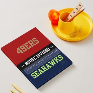 May include: A rectangular digital crochet blanket pattern document featuring a red section with the text 49ERS in gold and a navy blue section with the text SEAHAWKS in lime green. The center black band reads HOUSE DIVIDED and CROCHET BLANKET PATTERN.