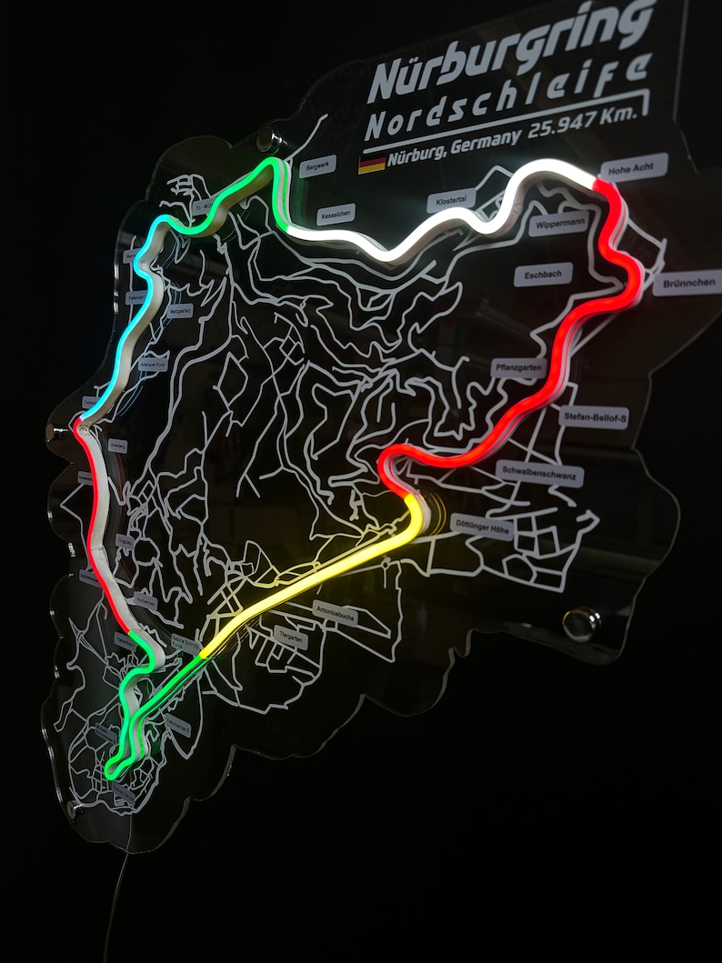 May include: A black acrylic map of the N&uuml;rburgring Nordschleife race track with a white outline of the track. The track is highlighted with neon green, yellow, and red lines. The map includes the name "N&uuml;rburgring Nordschleife" and the text "N&uuml;rburg, Germany 25.947 Km."