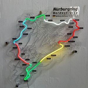 May include: A neon sign depicting the N&uuml;rburgring Nordschleife race track in Germany. The track is outlined in green, yellow, red, and white neon lights. The sign also includes the text "N&uuml;rburgring Nordschleife" and "N&uuml;rburg, Germany 25.347 Km."