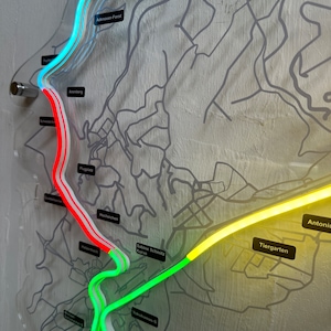 May include: A close-up of a map with a neon green, yellow, and red track marked on it. The track is labeled with names like "Sabine Schmitz Kurve", "Tiergarten", and "Antoniu".