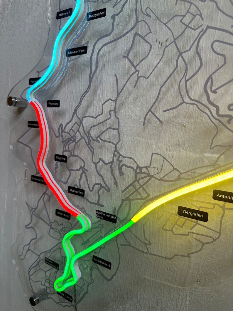 May include: A close-up of a map with a neon green, yellow, and red track marked on it. The track is labeled with names like "Sabine Schmitz Kurve", "Tiergarten", and "Antoniu".