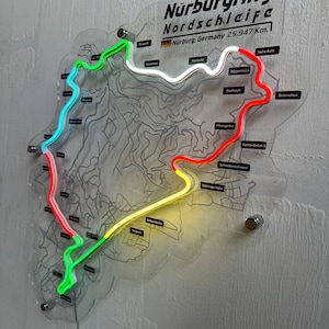 May include: A neon sign depicting the N&uuml;rburgring Nordschleife race track in Germany. The track is outlined in green, red, and yellow neon lights. The sign also includes the text "N&uuml;rburgring Nordschleife" and "N&uuml;rburg, Germany 25.947 Km."