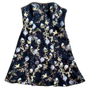 May include: A strapless black dress with a floral pattern. The dress features a fitted bodice and a flared skirt. The floral design includes white, yellow, and green accents. The top edge of the dress has a decorative trim.