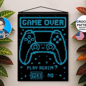 Può includere: Un arazzo nero con un design a uncinetto pixelato blu di un controller per videogiochi. Il testo GAME OVER appare in alto, con PLAY AGAIN? e le opzioni YES e NO in basso. Il design è sospeso tramite un'asta nera.