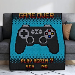 May include: A rectangular throw blanket featuring a pixelated video game controller graphic in black, grey, and blue. The text GAME OVER appears at the top, with PLAY AGAIN? YES NO displayed at the bottom in a retro, blocky, yellow and red font.