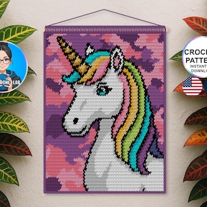 Op de afbeelding: Een gehaakte wandhanger met een eenhoorn met een regenboogmanen en hoorn, tegen een paarse achtergrond met roze wolken. De tekst "CROCHET PATTERN INSTANT PDF DOWNLOAD" wordt weergegeven. De wandhanger is omlijst met een houten staaf.
