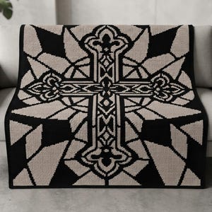 May include: A rectangular knit throw blanket featuring a large, centered cross motif with intricate fleur-de-lis detailing. The design is rendered in a high-contrast color scheme of solid black and light beige, creating a geometric, stained-glass effect.