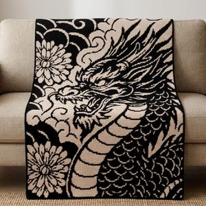 Peut inclure: Une couverture rectangulaire en crochet présentant un motif contrasté noir et crème. Le design affiche une grande tête de dragon détaillée avec des écailles et des moustaches fluides, entourée de nuages stylisés et de deux grandes fleurs de chrysanthème.