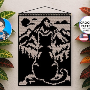 May include: A rectangular crochet wall hanging featuring a black silhouette of a cat sitting in the foreground. The background depicts a detailed mountain range and a sun in a light beige colour against a solid black backdrop, suspended by a black cord.