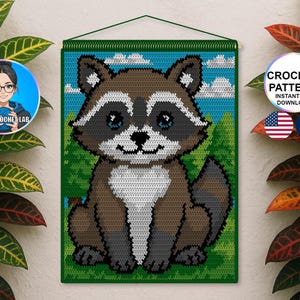 May include: A crocheted wall hanging depicting a raccoon. The raccoon is rendered in brown, white, and grey, with blue eyes, set against a green and blue backdrop. The text "CROCHET PATTERN INSTANT PDF DOWNLOAD" is visible.