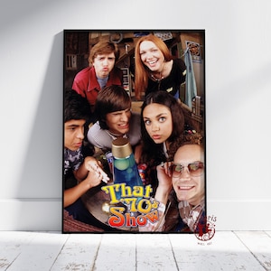 Puede incluir: Un póster enmarcado con el elenco de la serie de televisión "That '70s Show". La imagen muestra a seis jóvenes reunidos alrededor de una mesa con una lámpara de lava. El logotipo del programa se muestra de forma destacada en el centro.