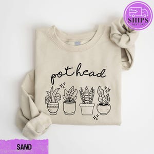 May include: A beige sweatshirt with the text "pothead" printed in black. Below the text are five black line drawings of potted plants.