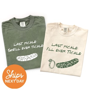 May include: Two crew neck t-shirts, one olive green and one cream. The olive shirt features white text reading LAST PICKLE SHE'LL EVER TICKLE above a pickle graphic. The cream shirt features dark green text reading LAST PICKLE I'LL EVER TICKLE.