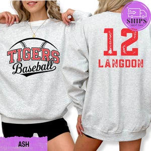 May include: Light gray sweatshirt with "TIGERS Baseball" in red and black lettering on the front. The back features the number "12" and the name "LANGDON" in red. The sweatshirt is a casual athletic style.