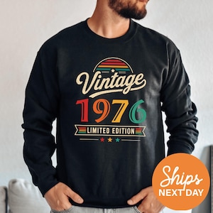 May include: A black long-sleeve sweatshirt featuring a graphic print with the text Vintage 1976 Limited Edition. The design includes a multi-colored semi-circle, the year 1976 in large red, orange, yellow, and green digits, and three small stars.