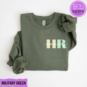 May include: A green sweatshirt with the text "HR" in colorful block letters and the word "nancy" written in cursive underneath.