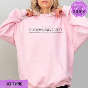 a woman wearing a pink hoodie that says custom university