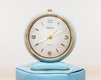 May include: A light blue vintage alarm clock with a white face and gold accents. The clock says "Saxony" and "Alarm" on the face.