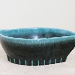 May include: A teal and black ceramic bowl with a scalloped edge. The bowl is glazed and has a gradient of color from teal to black.