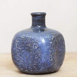 May include: A blue ceramic vase with a textured surface. The vase has a round body and a narrow neck.