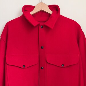 May include: A red long-sleeved shirt with a button-up front and two large pockets. The shirt has a classic workwear style.