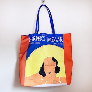 May include: A blue and red tote bag with a vintage Harper's Bazaar magazine cover featuring a woman with dark hair and a white dress. The cover reads "Harper's Bazaar" and "January 1932".