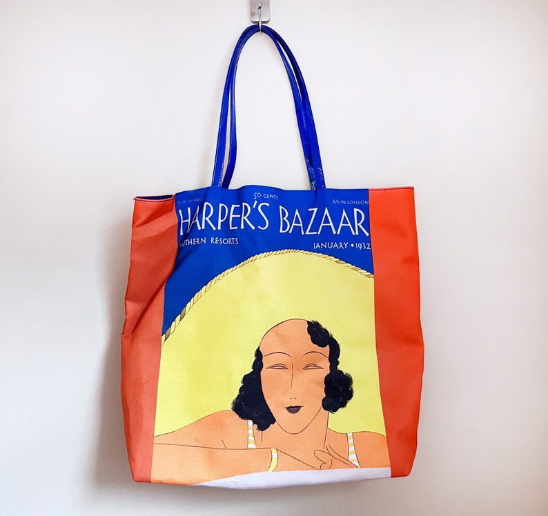 May include: A blue and red tote bag with a vintage Harper's Bazaar magazine cover featuring a woman with dark hair and a white dress. The cover reads "Harper's Bazaar" and "January 1932".