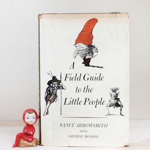 May include: A vintage book titled "A Field Guide to the Little People" by Nancy Arrowsmith with George Moore. The cover features illustrations of three whimsical characters with red hats.
