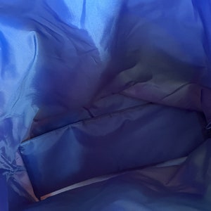 May include: Inside view of a blue nylon tote bag with a zippered pocket. The bag is empty and the fabric is smooth.