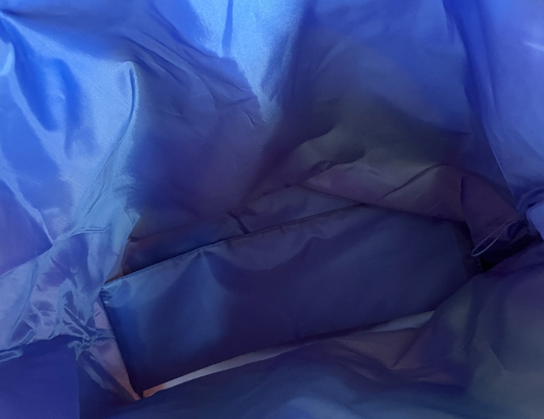 May include: Inside view of a blue nylon tote bag with a zippered pocket. The bag is empty and the fabric is smooth.