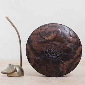 May include: A dark brown wooden coaster with a carved floral design. The coaster is round and has a slightly raised edge.