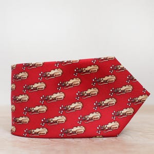 May include: A red tie with a repeating pattern of beige golf club illustrations. The tie is made of a smooth fabric and is displayed on a light-coloured surface. The golf club design adds a touch of novelty to the accessory.