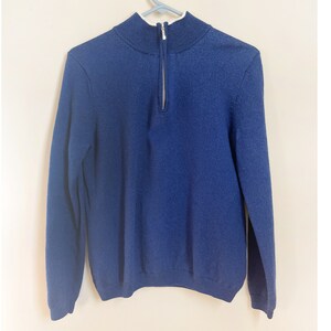 May include: A navy blue sweater with a quarter-zip closure and a white inner collar. The sweater is made of a soft material and is hanging on a white hanger against a light background.