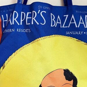 May include: A blue and red tote bag with the text "Harper's Bazaar" in white. The bag features a yellow sombrero with a brown rope trim and a cartoon illustration of a man's face. The text "50 cents", "Southern Resorts", "4/6 in London", and "January 1932" is also printed on the bag.