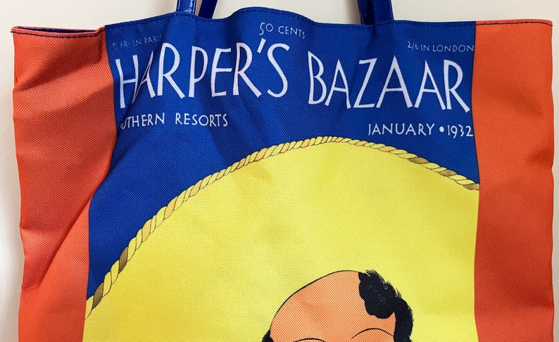 May include: A blue and red tote bag with the text "Harper's Bazaar" in white. The bag features a yellow sombrero with a brown rope trim and a cartoon illustration of a man's face. The text "50 cents", "Southern Resorts", "4/6 in London", and "January 1932" is also printed on the bag.