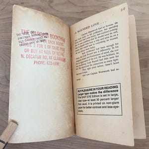 Op de afbeelding: Open boek met tekst op verouderd papier. De tekst bevat "A Wounded Love" en een beschrijving van het verhaal. Het boek heeft ook een stempel van "The Book End Bookstore" met adres en telefoonnummer.