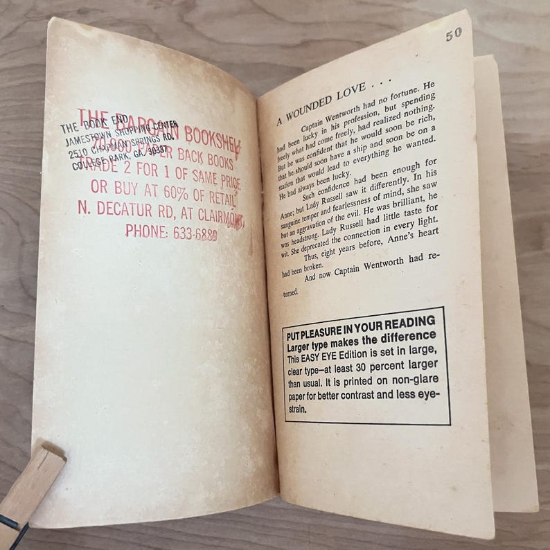 Op de afbeelding: Open boek met tekst op verouderd papier. De tekst bevat "A Wounded Love" en een beschrijving van het verhaal. Het boek heeft ook een stempel van "The Book End Bookstore" met adres en telefoonnummer.