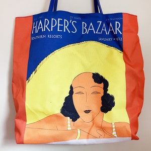 May include: A red, white, and blue tote bag with a vintage illustration of a woman wearing a swimsuit and a large sun hat. The bag features the text "Harper's Bazaar" and "Southern Resorts" in a blue font. The text "January 1932" is also visible in the bottom right corner.