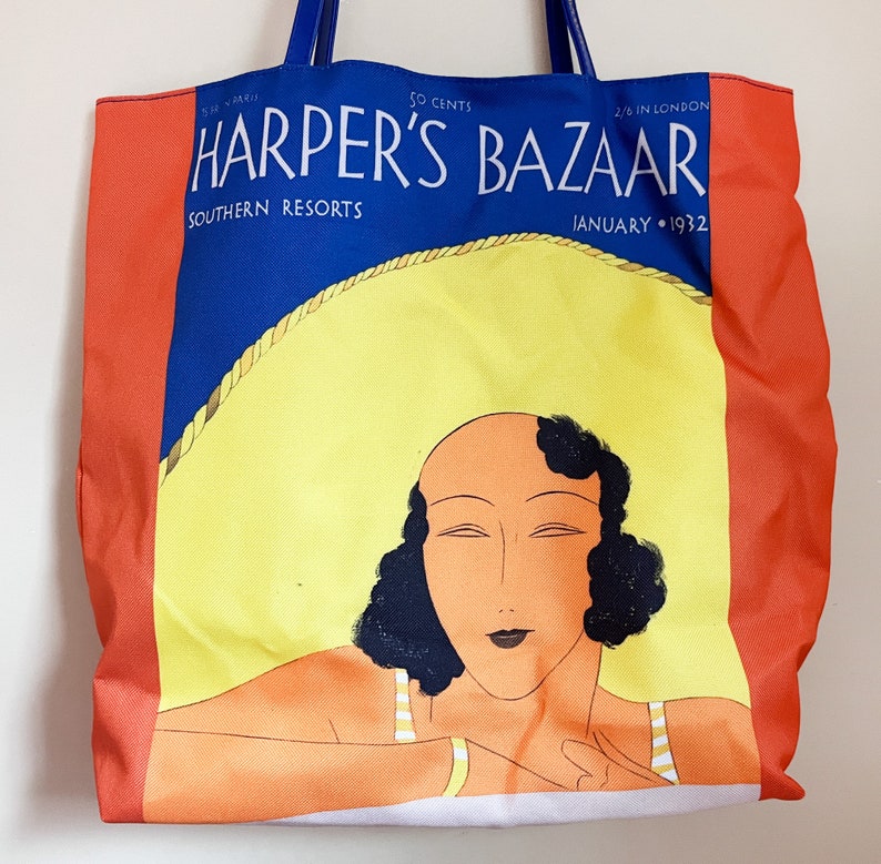 May include: A red, white, and blue tote bag with a vintage illustration of a woman wearing a swimsuit and a large sun hat. The bag features the text "Harper's Bazaar" and "Southern Resorts" in a blue font. The text "January 1932" is also visible in the bottom right corner.