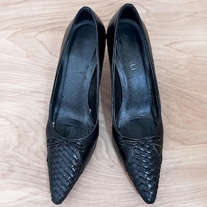 May include: A pair of black leather pointed-toe heels with a woven detail on the toe. The heels are approximately 3 inches tall.