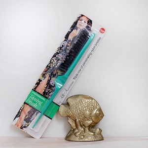 May include: A teal plastic teasing brush with black bristles, packaged with a woman on the front. The package says "Professional Teasing Brush by All-American Triple row of penetrating nylon bristles 100".